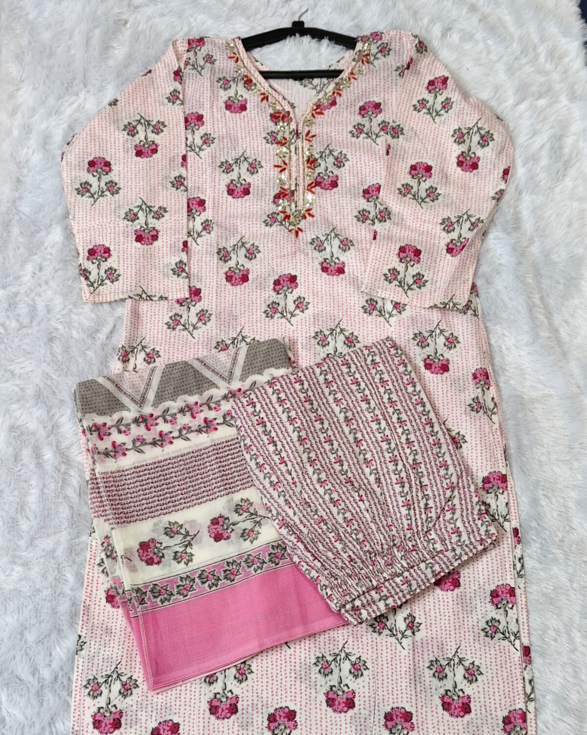 Woman wearing elegant white and pink floral Cambric Cotton suit set with kurta, printed pant, and dupatta – ethnic wear for women.