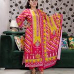 Woman wearing vibrant yellow and pink embroidered muslin suit set with floral motifs and matching printed dupatta – festive ethnic wear.
