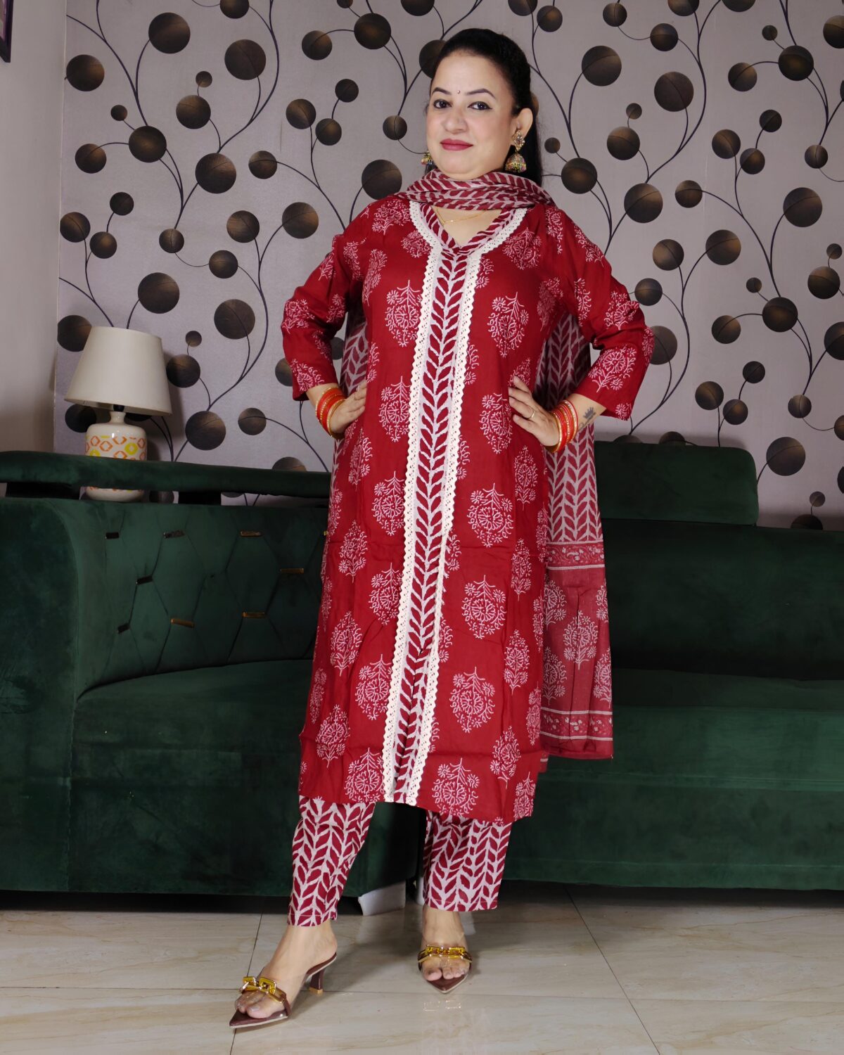 Woman wearing a premium rust handblock printed cotton suit set featuring lace-detailed V-neck kurta, printed pants, and matching dupatta.