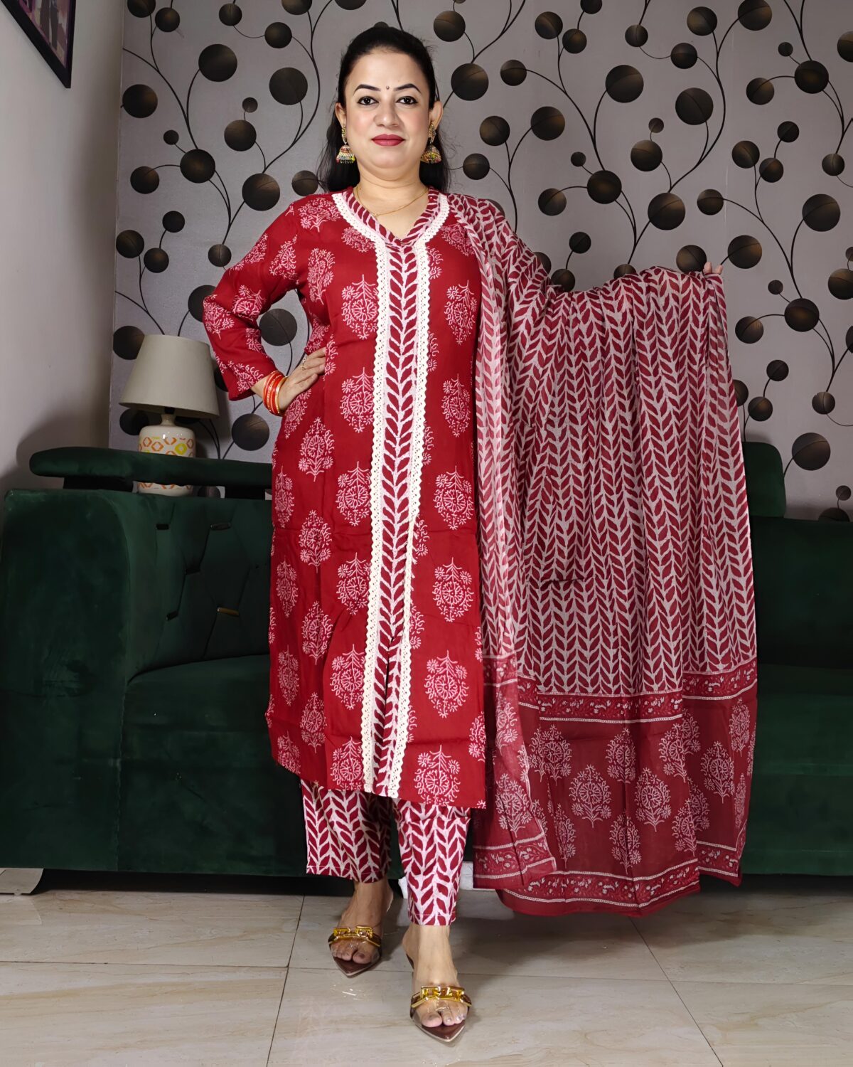 Woman wearing a premium rust handblock printed cotton suit set featuring lace-detailed V-neck kurta, printed pants, and matching dupatta.